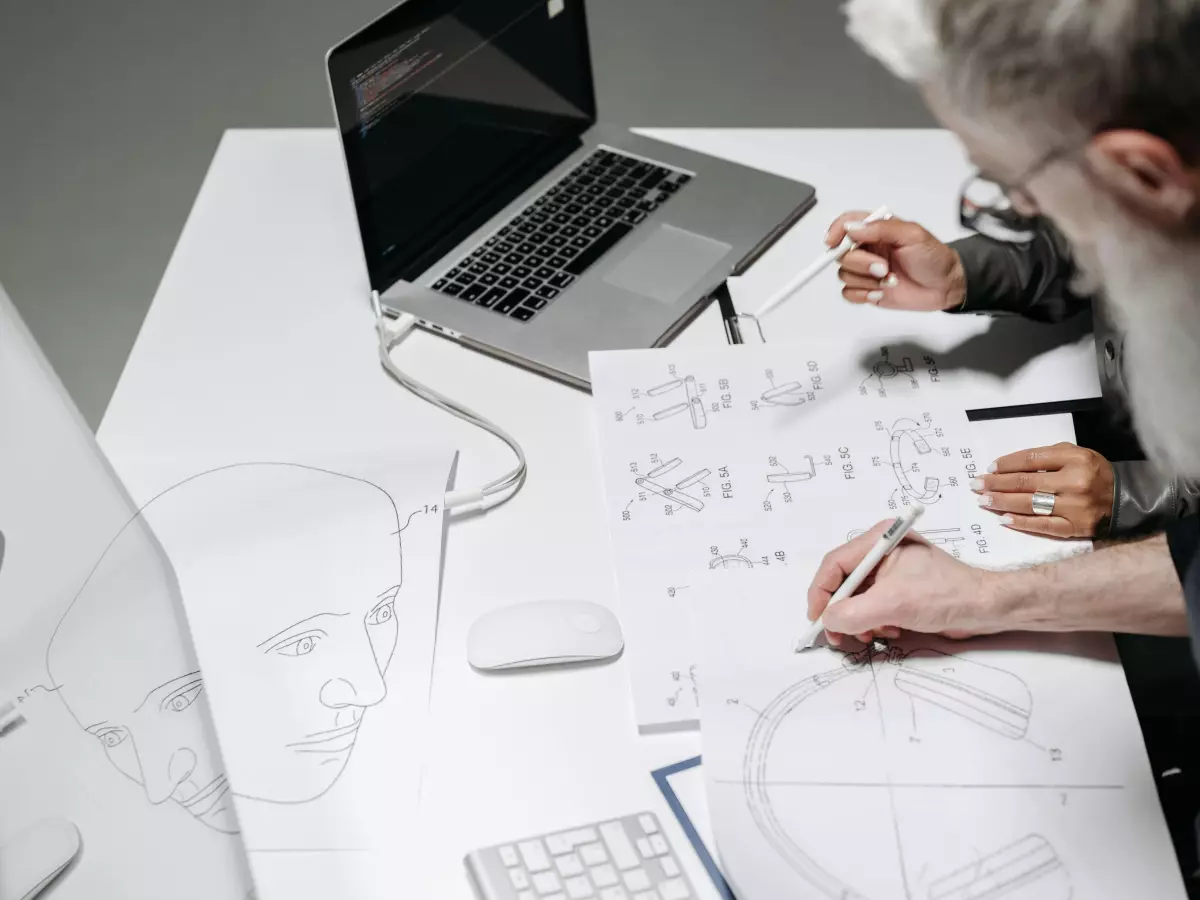 Two people are working together on a diagram at a desk with a laptop and other office supplies.